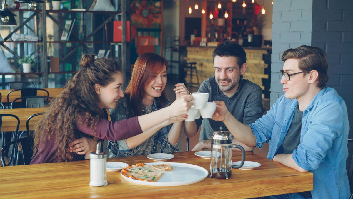 Friends toasting with cups of coffee around a table